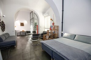 A modern interior with a bed, sofa, dining table, chairs, and a small kitchen area. - GuestHost - A practical and welcoming 50 square meters open-plan loft, perfect for two people, located on the ground floor of an elegant building with a courtyard.The property is located in the Prati district, one of Rome's most charming areas: our guest (Rome)