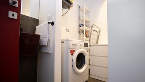 A compact laundry area with a washing machine, a drying rack, and a shelf with laundry supplies. - GuestHost - A practical and welcoming 50 square meters open-plan loft, perfect for two people, located on the ground floor of an elegant building with a courtyard.The property is located in the Prati district, one of Rome's most charming areas: our guest (Rome)