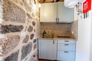 A kitchen with a stone wall, a sink, and light-colored cabinets. - Casa da Raposa by CVL (Castro-Laboreiro, Melgaço)