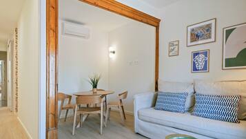 Ein Zimmer mit einer holzrahmenverzierten Tür, einem Esstisch mit Stühlen, einer Couch mit gemusterten Kissen und an der Wand befestigter Kunst.