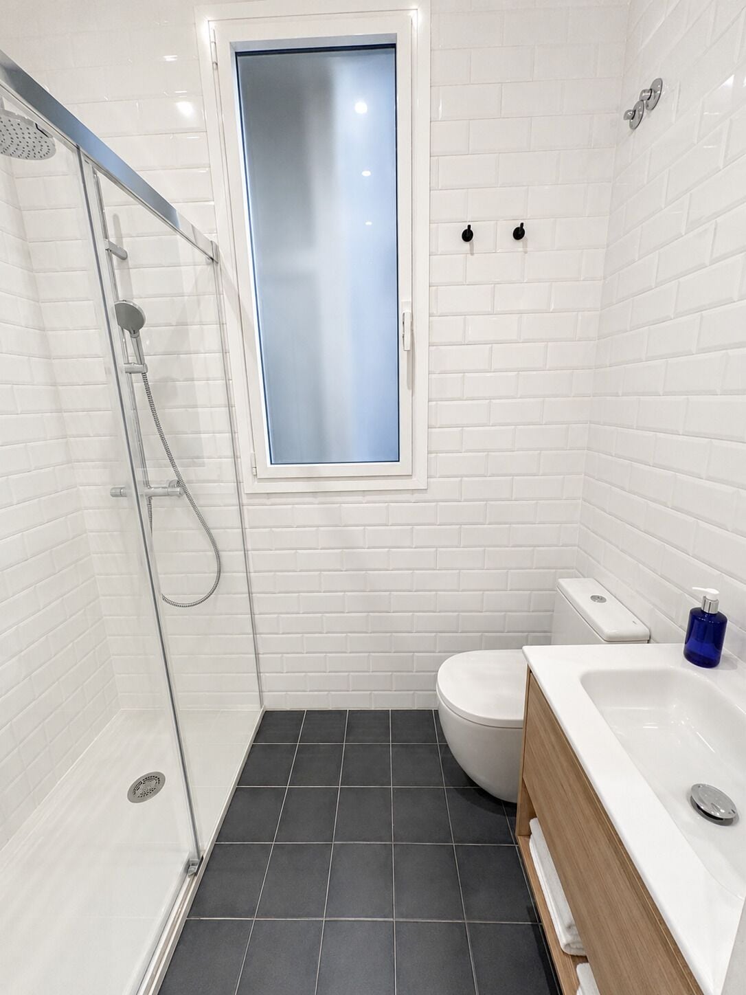 Un baño moderno con ducha envuelta en vidrio, inodoro y lavabo con tocador de madera.