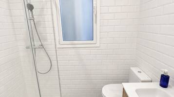 Un baño moderno con ducha envuelta en vidrio, inodoro y lavabo con tocador de madera.