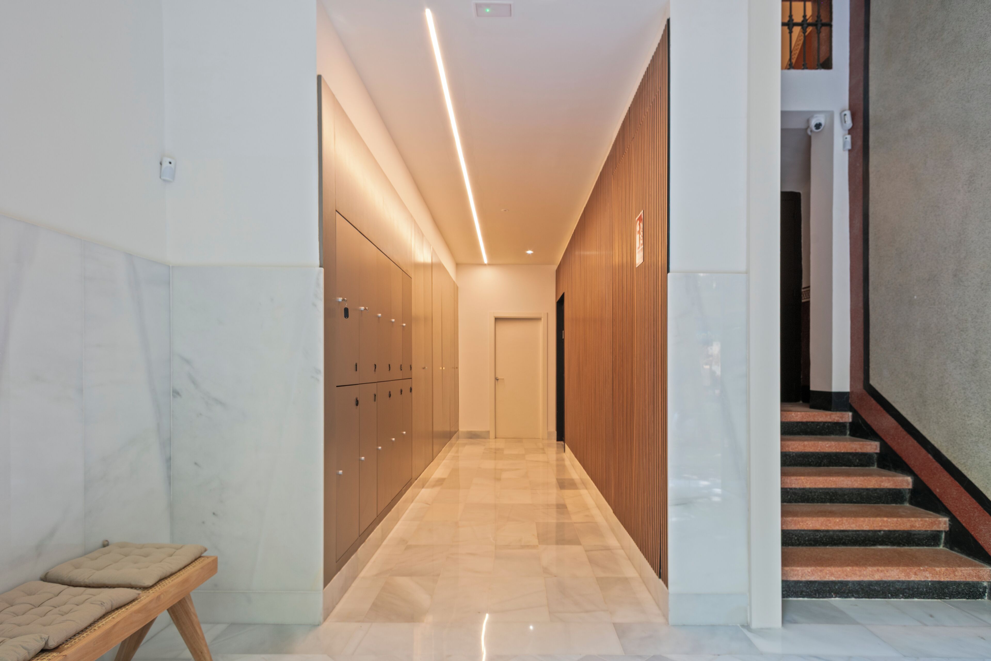A modern hallway with lockers, a bench, and a staircase.