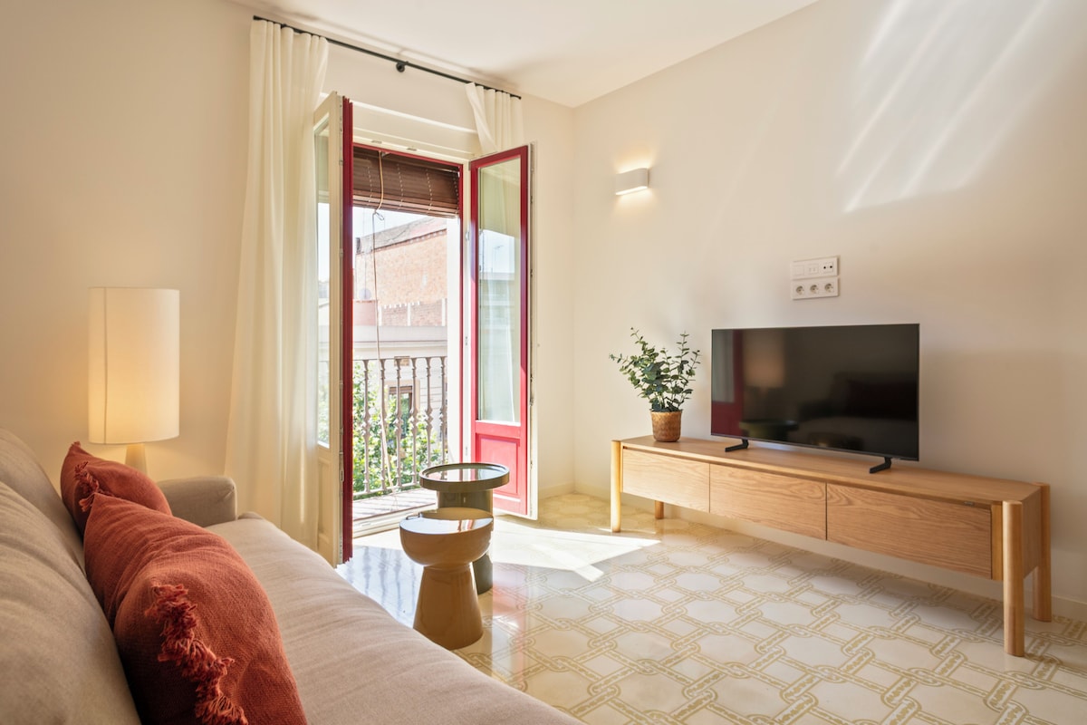 Una sala de estar con un sofá, un televisor sobre un mueble de madera, una lámpara y una planta en maceta.