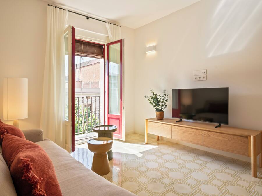 Una sala de estar con un sofá, un televisor sobre un mueble de madera, una lámpara y una planta en maceta.