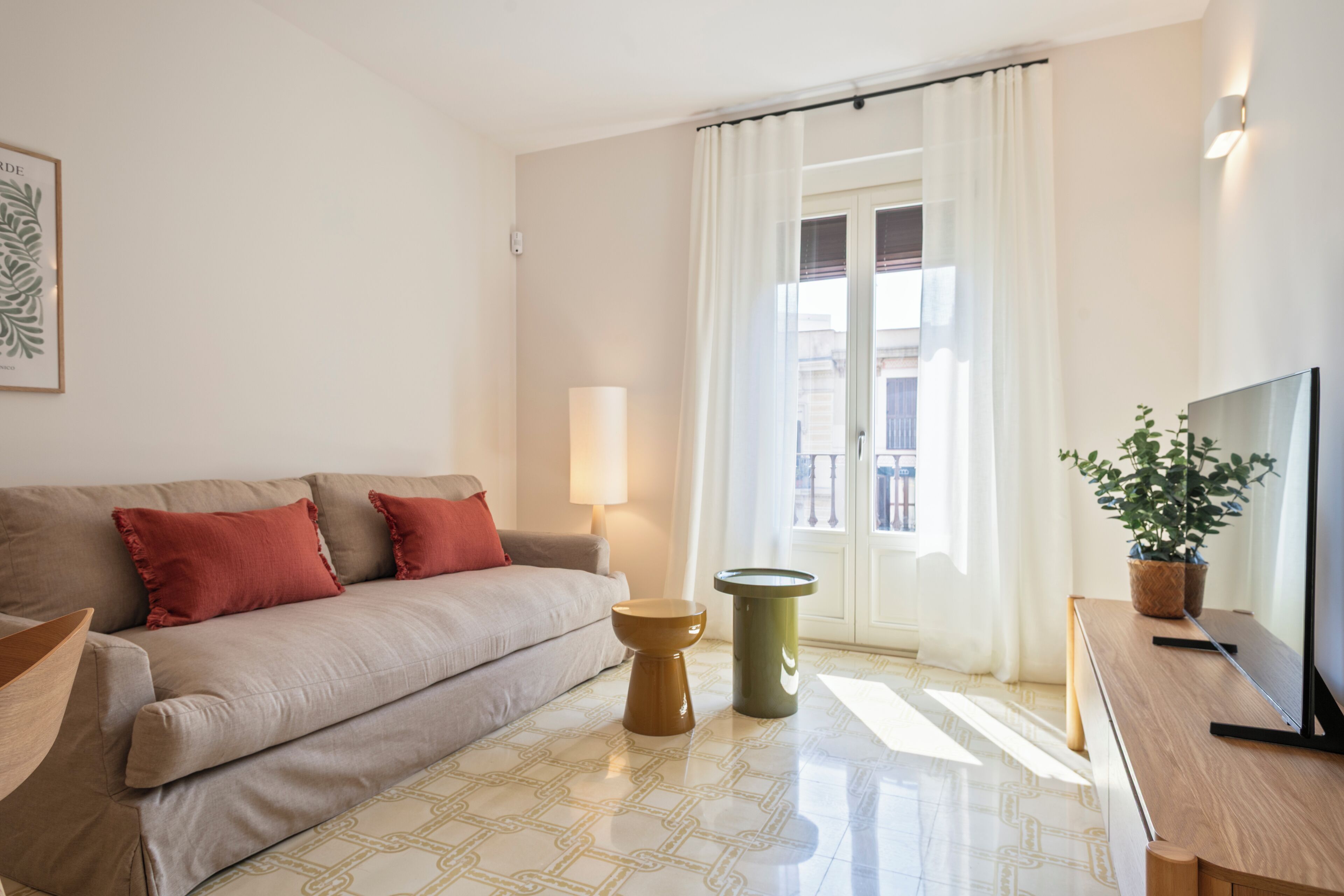 Un salon moderne comprenant un canapé, une table basse, une table d’appoint, une lampe, un téléviseur et une plante en pot.