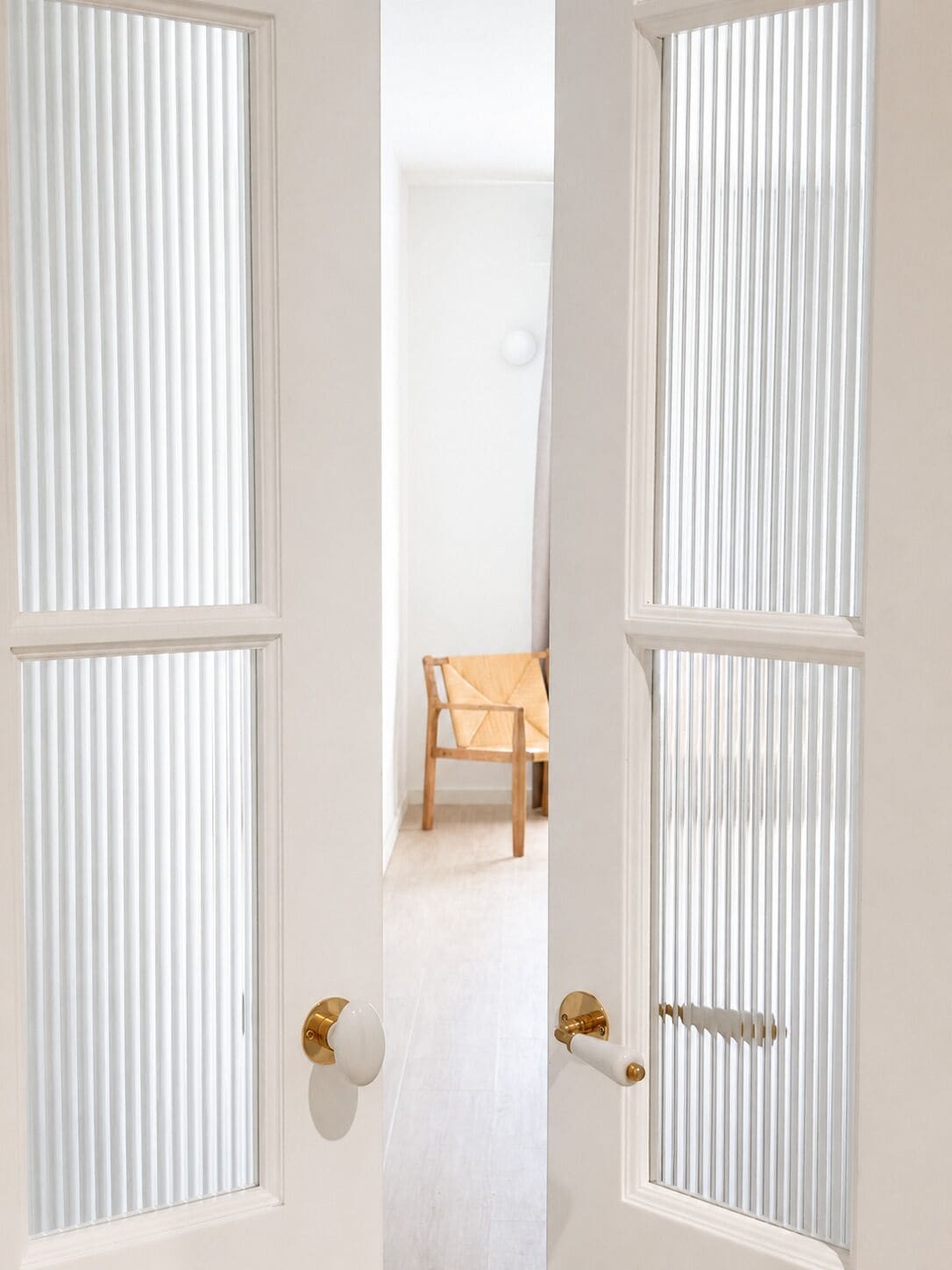 Una puerta con persianas verticales, una silla de madera y una pared blanca.