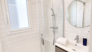 A modern bathroom with a glass-enclosed shower, a white sink with a mirror, and a window.
