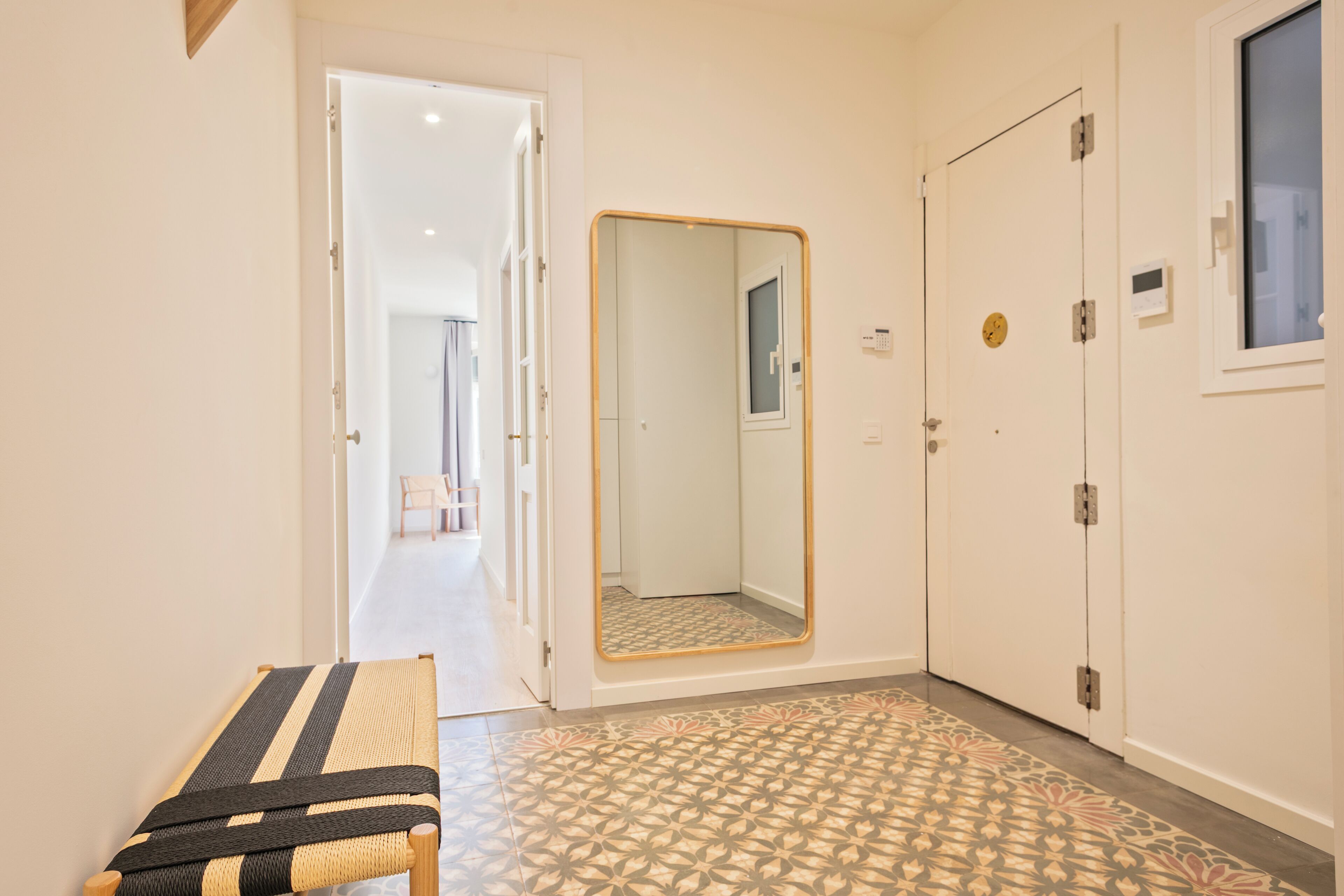 Un couloir avec un banc, un miroir et une porte dotée d’une fenêtre.