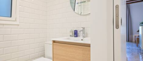 A modern bathroom with white subway tiles, a white toilet, a wooden vanity with a sink, and a mirror above the vanity.