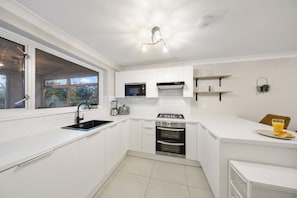 Una cocina moderna con armarios blancos, horno empotrado, microondas y estufa a gas.