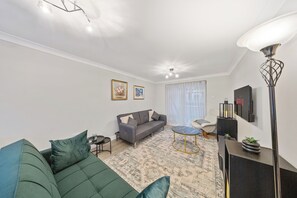 Una sala de estar moderna con un sofá verde, un sofá gris, un tapete estampado, una mesita redonda y una lámpara de pie.