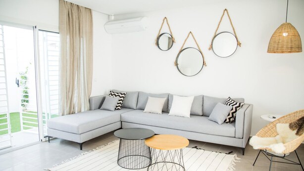 Una sala de estar moderna con un sofá seccional gris, dos mesitas auxiliares y una silla de mimbre.