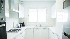 Una cocina moderna con armarios blancos, una estufa a gas, una cafetera y una ventana sobre el fregadero.