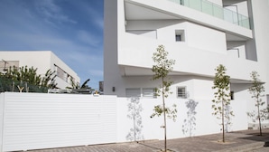Un edificio moderno con fachada blanca, entrada protegida por una reja y camino de entrada pavimentado.