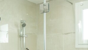 Un área de ducha con paredes de vidrio, con un cabezal de ducha de mano y un grifo instalado en la pared.