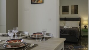 En matplats med ett bord dukat för fyra personer, en tavla på väggen och en säng i bakgrunden.