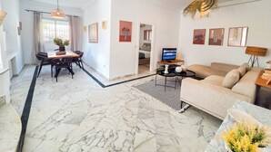 A modern living room with a marble floor, a sofa, a dining area with chairs, and a TV.