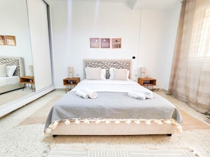 Ein modernes Schlafzimmer mit einem großen Bett, Nachttischen, einem Spiegel und Bildern an der Wand.