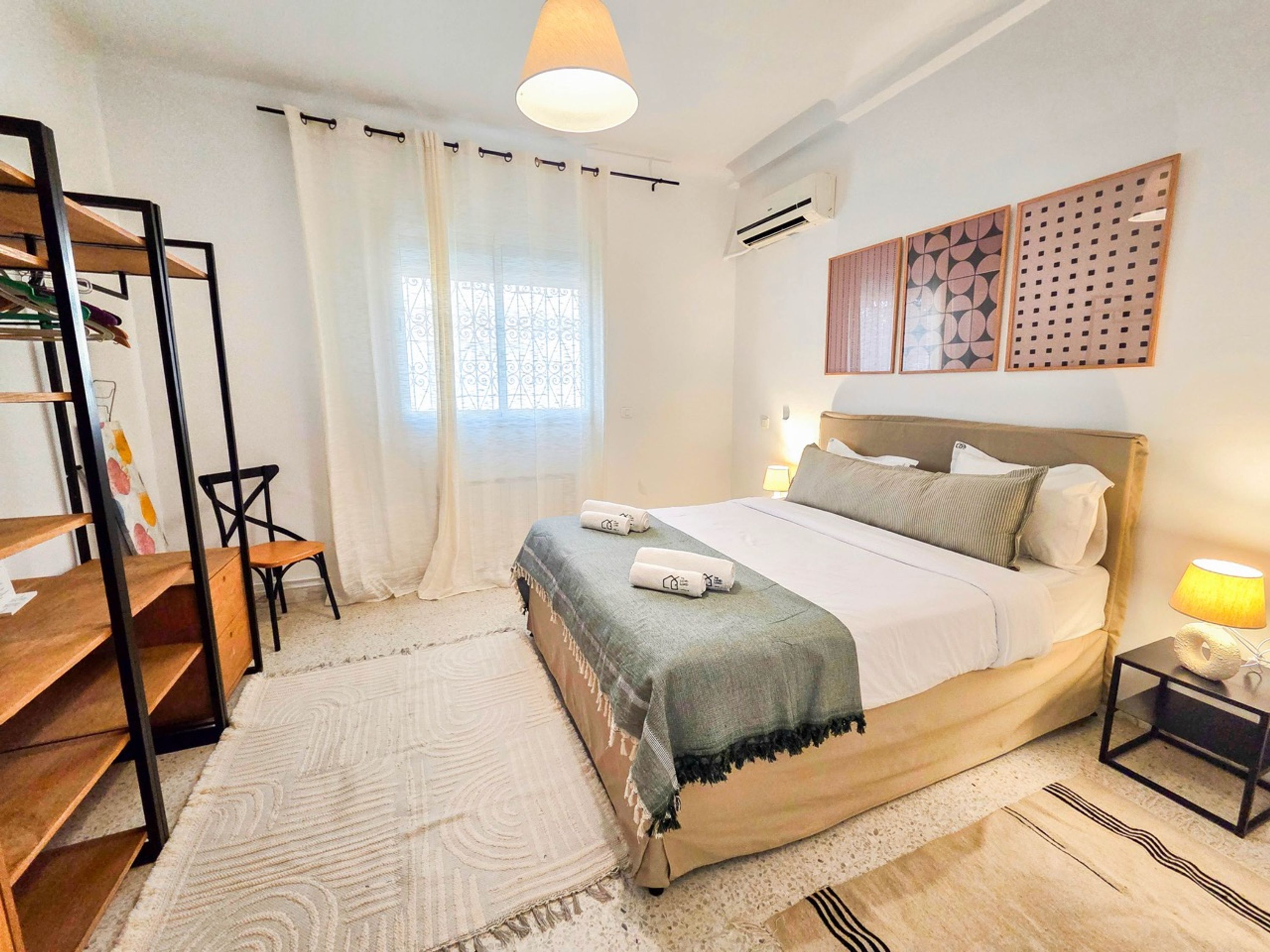 A bedroom with a bed, a desk, a chair, a lamp, and a window with curtains.