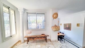 A room with a marble floor, a bench, a window with metal bars, and a wall with a hat and a framed picture.