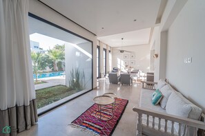 Un salon moderne doté d’une grande porte-fenêtre coulissante, d’un tapis coloré, d’un canapé blanc et d’un coin repas à l’arrière-plan.