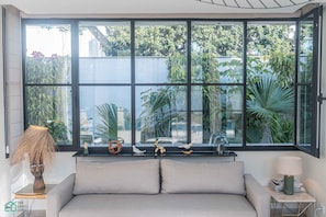 Ein modernes Wohnzimmer mit großem Fenster, einer Couch, einem Beistelltisch mit Lampe und Dekoration.