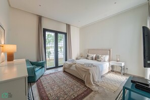 Ein Hotelzimmer mit Bett, Schreibtisch, Fernseher, einer Couch und einem großen Fenster mit Vorhängen.