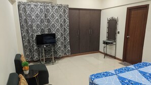 A bedroom with a bed, a TV on a stand, a wardrobe, and a small table with a mirror.