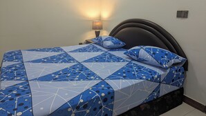 A bed with a geometric patterned bedspread and matching pillows, a bedside lamp, and a dark headboard.