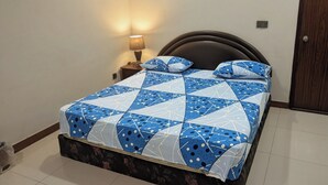 A bed with a geometric patterned bedspread, a nightstand with a lamp, and a wooden headboard.