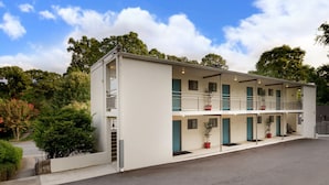 Um motel de dois andares com corredor central, quartos individuais em cada andar e área de estacionamento na frente.