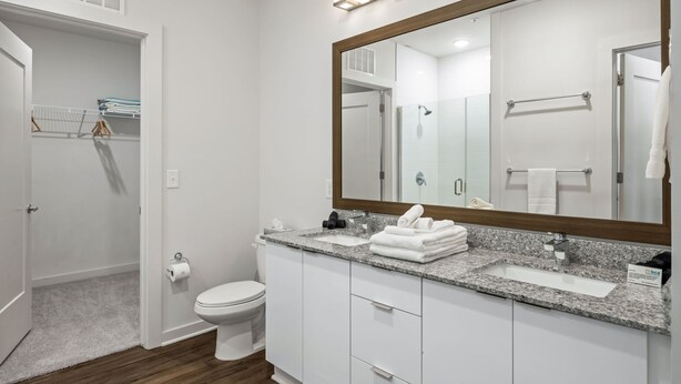 Une salle de bain moderne avec un grand miroir, des meubles blancs, un comptoir en granit et un espace douche.