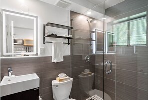 Ett modernt badrum med en dusch som är avskärmad med glasväggar, ett vitt handfat och en toalett.