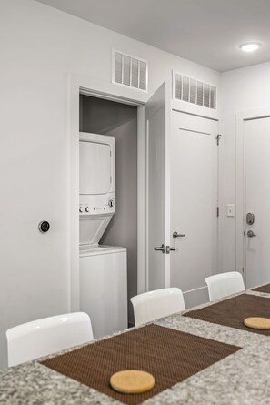 A hotel room with a dining area, a washer and dryer, and a door with a handle. - (S2BA) Modern 2-BR, Walkable in Midtown, 1 Block from MARTA (Atlanta)
