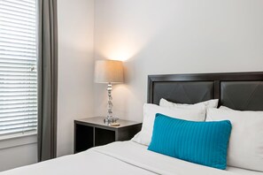 A neatly made bed with white and blue pillows, a bedside lamp, and a nightstand. - (S2BA) Modern 2-BR, Walkable in Midtown, 1 Block from MARTA (Atlanta)