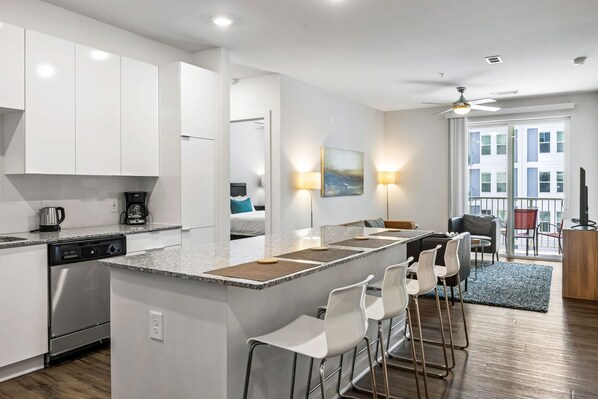 A modern kitchen with white cabinets, a built-in dishwasher, and a central island with bar stools. - (S2BA) Modern 2-BR, Walkable in Midtown, 1 Block from MARTA (Atlanta)