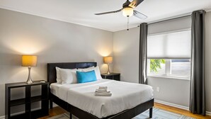 A hotel room with a bed, two bedside tables with lamps, a ceiling fan, a window with curtains, and a view of the outside. - (B2bF) Quick + Easy Virtual Check In w/ Free Parking (Atlanta)