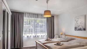 Un dormitorio con cama, cortinas, lámpara y un cuadro.