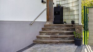 Un conjunto de escalones de piedra que llevan a una puerta, un buzón negro y una planta en maceta en el suelo.