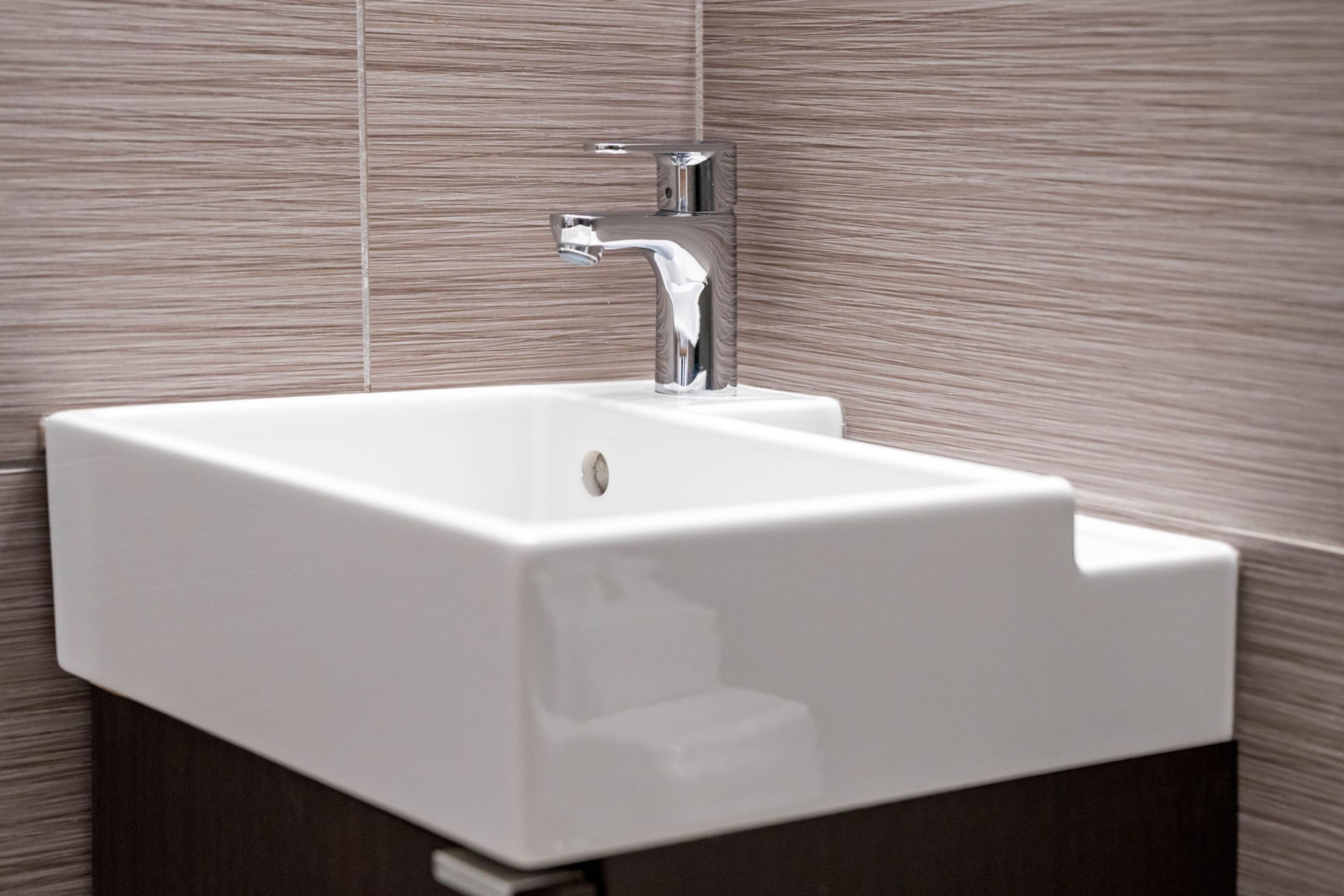A modern bathroom with a white sink and chrome faucet against a textured wall.