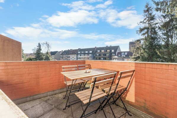 Una terraza en la azotea con una mesa y sillas de madera, un muro de ladrillo y vistas a edificios residenciales.