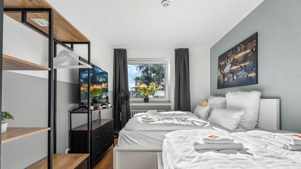 Ein modernes Schlafzimmer mit einem großen Bett, einem Holzschrank, einem Schreibtisch mit Computer und einem Fenster mit Vorhängen.