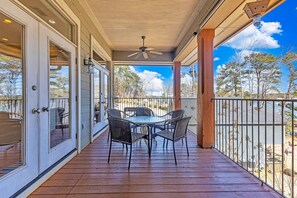 A covered outdoor patio with a table and chairs, a ceiling fan, and a view of trees and sky.