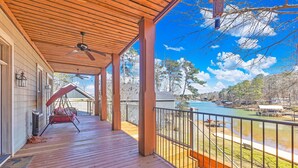 Terraza de madera con ventilador de techo, una silla colgante y vista a un lago y zona de embarcadero.
