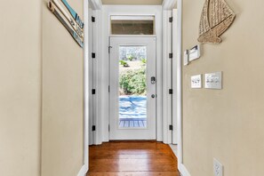 A hallway with a wooden floor, a white door with a glass panel, and a view of a backyard with greenery. - Sailor's Cove by Lake Martin Vibe, 3 bedrooms, 2.5 baths, pets ok! (Dadeville)