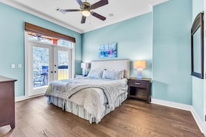 A bedroom with a bed, a ceiling fan, a nightstand, a lamp, and a window with a view of trees. - Sailor's Cove at Lake Martin, 3 bedrooms, 2.5 baths, pets ok! (Dadeville)