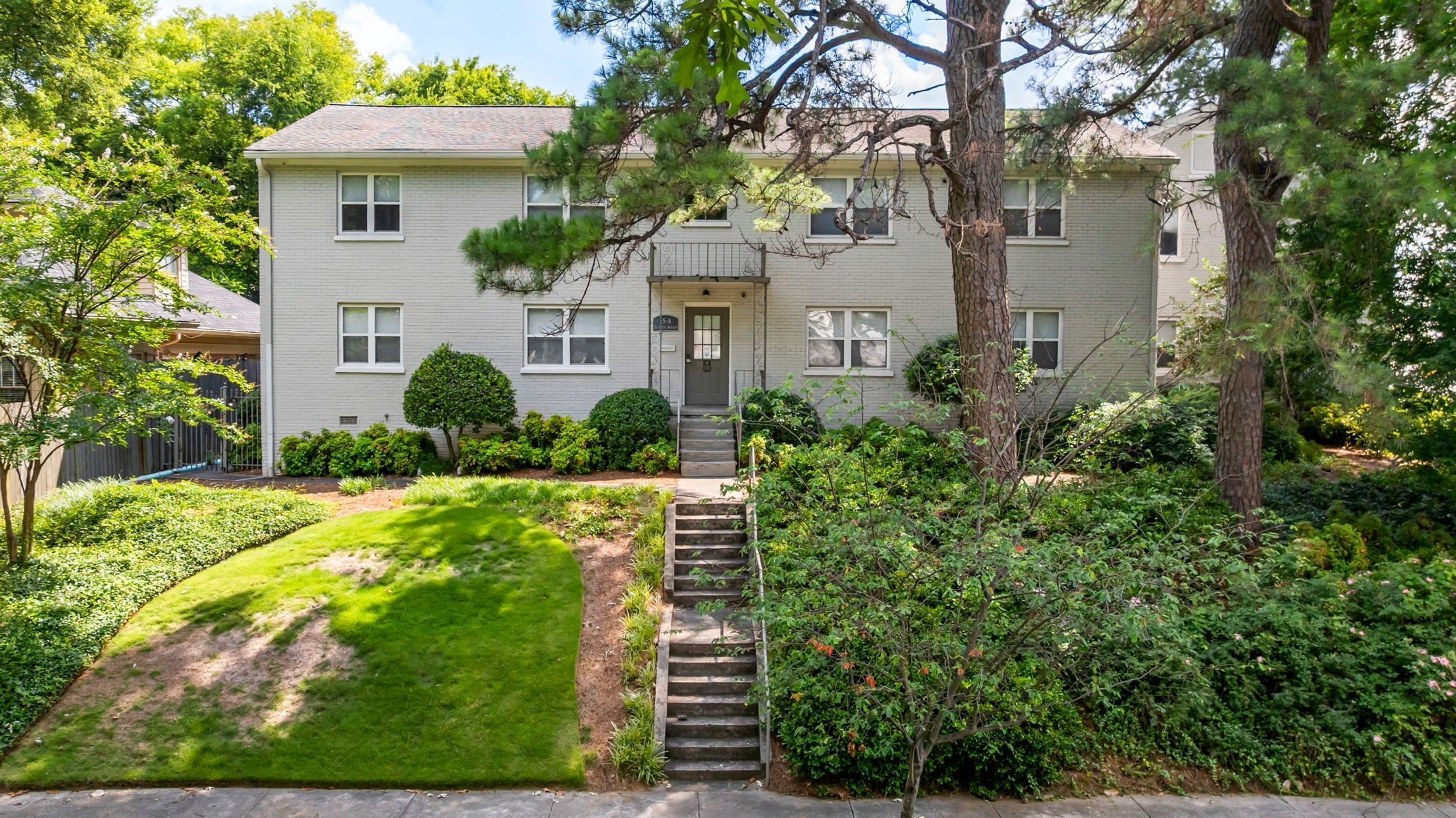 A two-story residential building with a front entrance, a small front yard, and a staircase leading to the entrance.