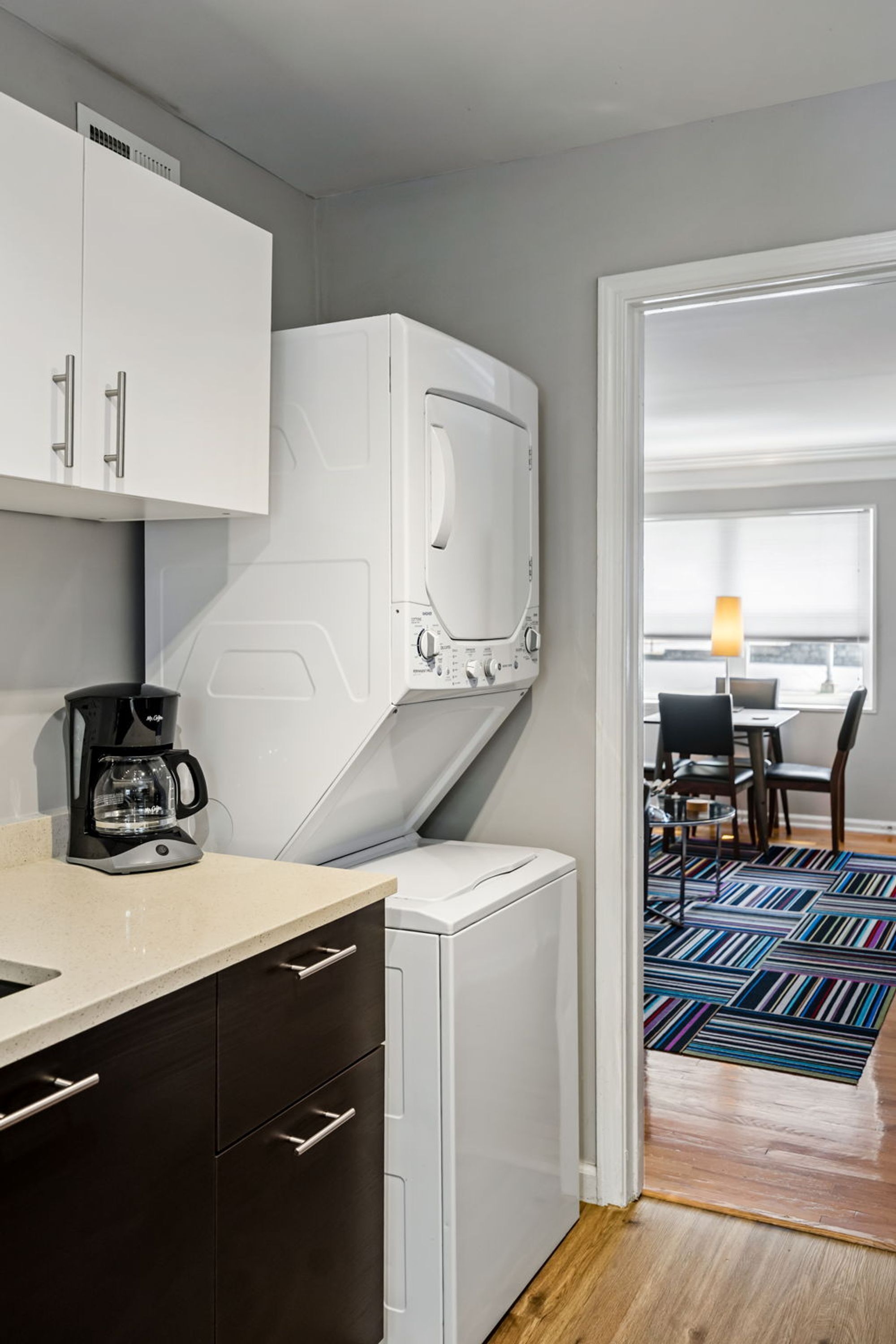 A compact kitchen with a microwave, coffee maker, and a small refrigerator. A dining area with a table and chairs is visible through an open door.
