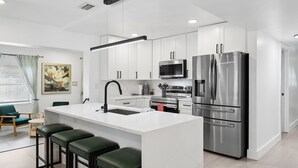 A modern kitchen with white cabinets, stainless steel appliances, and a central island with bar stools. - Sunny Terrace • Pool  Hot Tub • B-Ball CT•  Near Busch Gardens & USF • Sleeps 10 (Tampa)